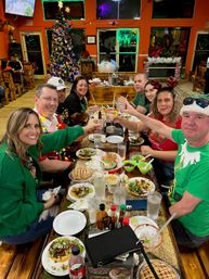 Eight friends toasting over tacos and margaritas at a festive, colorful casual Mexican restaurant interior with a decorated Christmas tree, holiday sweaters and twinkling lights.