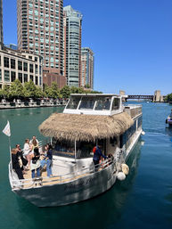 Thatched roof leisure boat on the Chicago River with people on deck and downtown skyscrapers under a bright blue sky