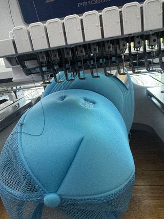 Close-up of a multi-needle embroidery machine stitching bright blue foam-front trucker caps with mesh backs, black thread visible