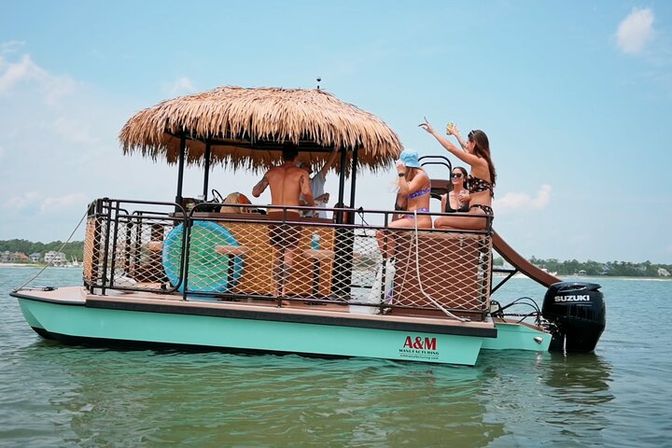 Group of friends on a turquoise pontoon boat with a thatched tiki-roof bar and rear water slide, enjoying drinks on a sunny day in calm coastal waters