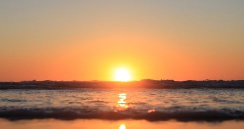 Coastal sunset seascape with the golden sun sinking at the ocean horizon, warm orange sky and shimmering reflections on gentle waves.