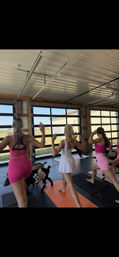 Group of women practicing goat yoga on colorful mats in a bright barn-style studio with glass garage doors and a rural farm view