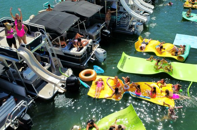 Aerial view of a sunny lake party with pontoon boats, slides and colorful inflatable loungers with people relaxing on the water