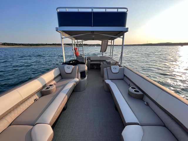 Pontoon boat interior with plush cushioned lounge seating, built‑in cup holders and upper-deck canopy cruising on calm lake waters at sunset