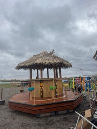 Thatched-roof tiki bar on a wooden floating deck with colorful stools at an overcast marina