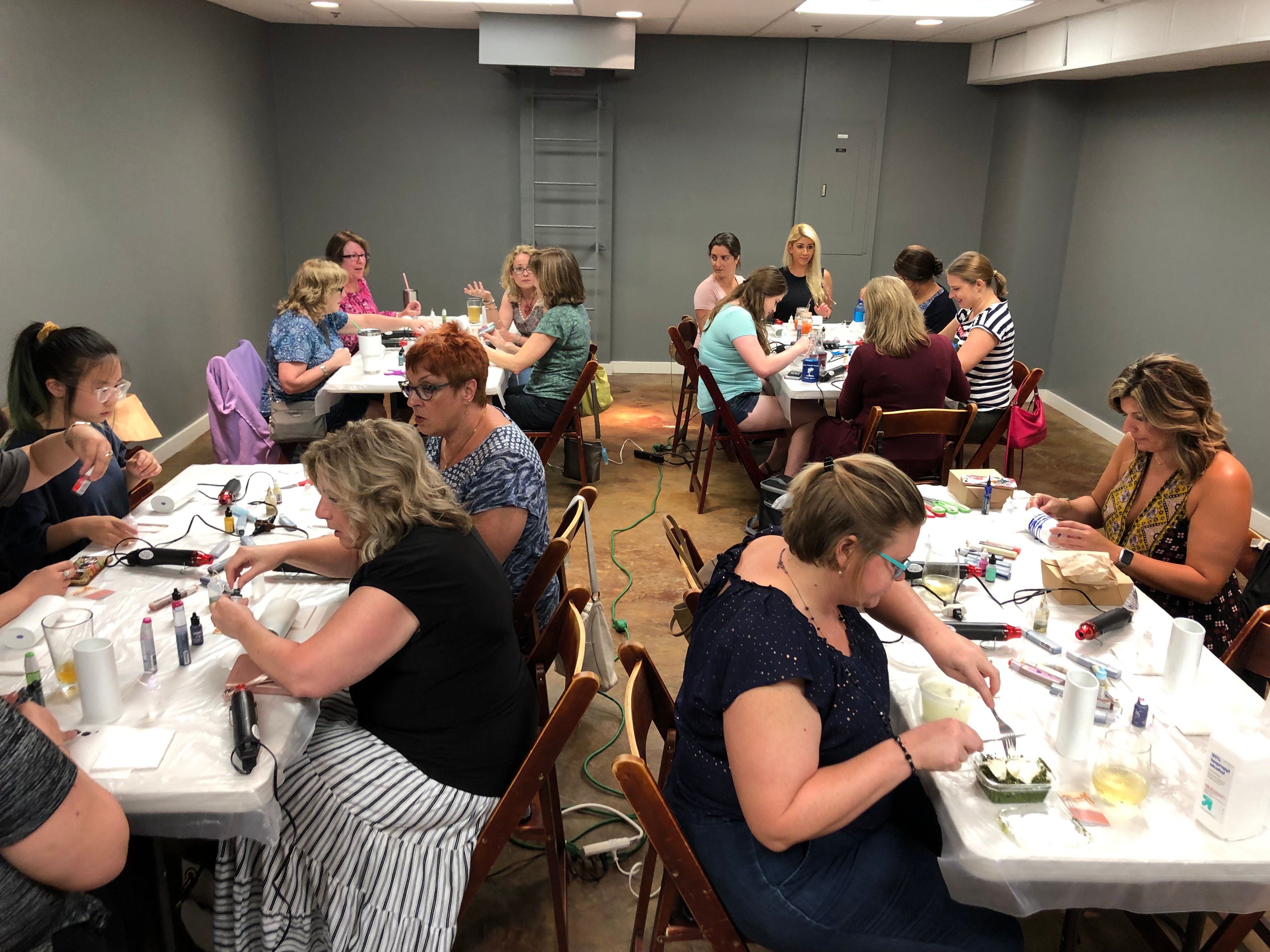 Hands-on DIY craft workshop in a community room — women seated at tables with paints, glue guns and tools, chatting and working on small projects