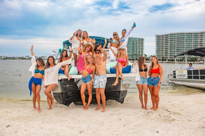 Smiling group of friends partying on a beached pontoon boat at a sunny coastal beach, wearing swimsuits and holding drinks with waterfront condos in the background