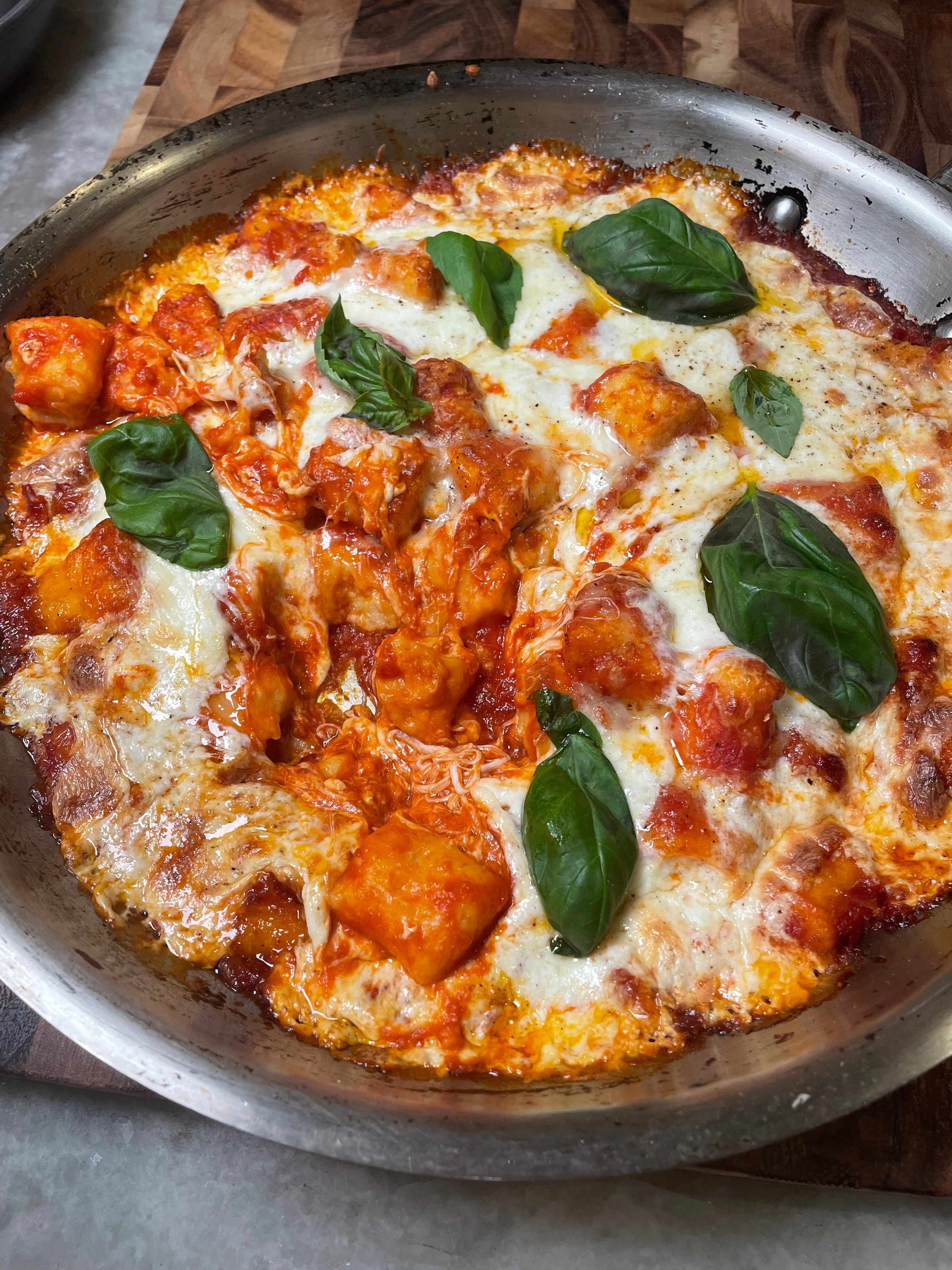 Skillet-baked gnocchi in rich tomato sauce with bubbling mozzarella and fresh basil leaves, served in a rustic pan on a wooden board