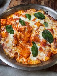 Skillet-baked gnocchi in rich tomato sauce with bubbling mozzarella and fresh basil leaves, served in a rustic pan on a wooden board