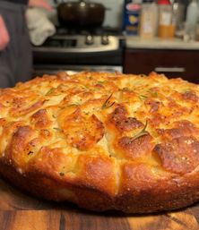 Mouthwatering close-up of golden rosemary focaccia with blistered, salty crust resting on a wooden board in a home kitchen