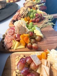 Close-up of gourmet charcuterie boards on wooden serving planks with sliced cheeses, prosciutto, crackers, red and green grapes, dried apricots and almonds — colorful party appetizer display.