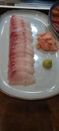 Close-up of a long row of thinly sliced white-fish sashimi on a ceramic plate, served with pickled ginger and a bright green wasabi dollop — Japanese sushi-style dish.