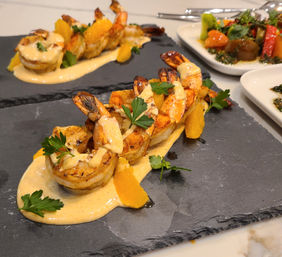 Grilled shrimp appetizer drizzled with creamy citrus sauce, orange segments and parsley on a black slate serving board — zesty seafood dish at a modern restaurant