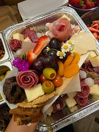 Gourmet charcuterie box with prosciutto roses, salami rosettes, assorted cheeses, grapes, strawberries, green olives, dried apricots, crackers and edible flowers — colorful party platter.