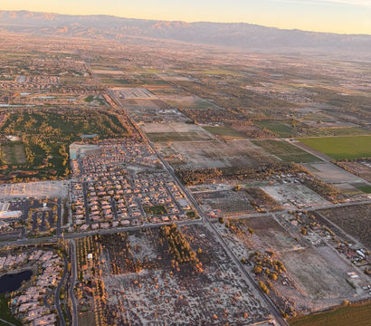 Sunset-lit aerial view of a sprawling valley featuring residential neighborhoods with pools and a golf course, patchwork farmland, straight grid roads, and a distant mountain range.