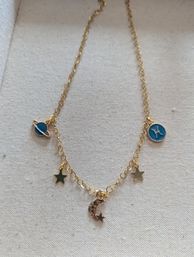 Delicate gold charm necklace with crescent moon, tiny star charms and blue enamel planet and Pisces discs on beige fabric background
