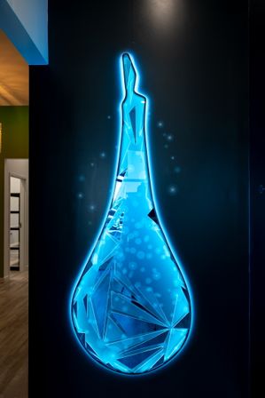 Futuristic neon-blue LED teardrop wall art with geometric crystal facets mounted on a dark wall in a modern interior hallway