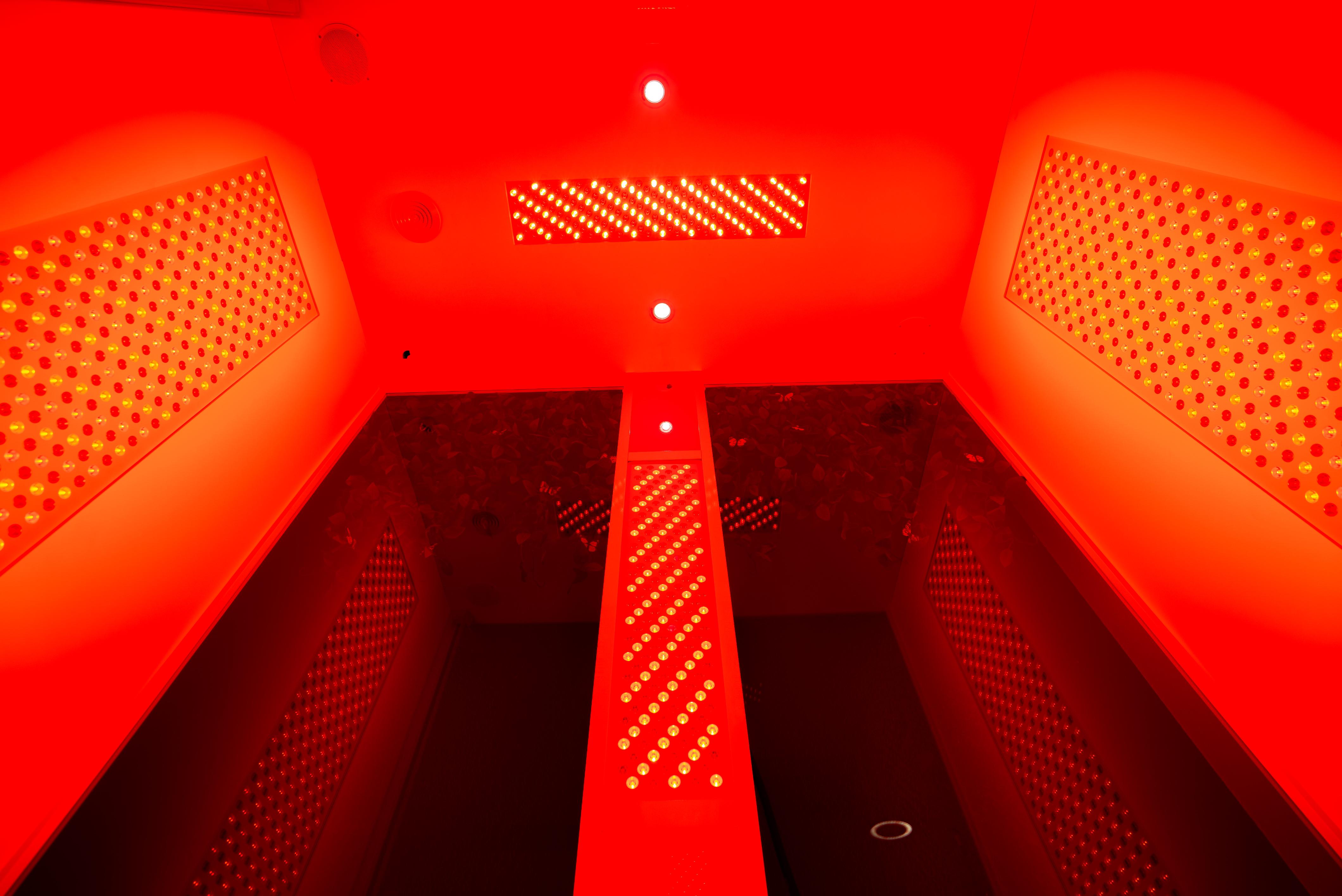 Vibrant red-light therapy chamber interior with ceiling and wall LED panels and reflective glass, viewed looking up.