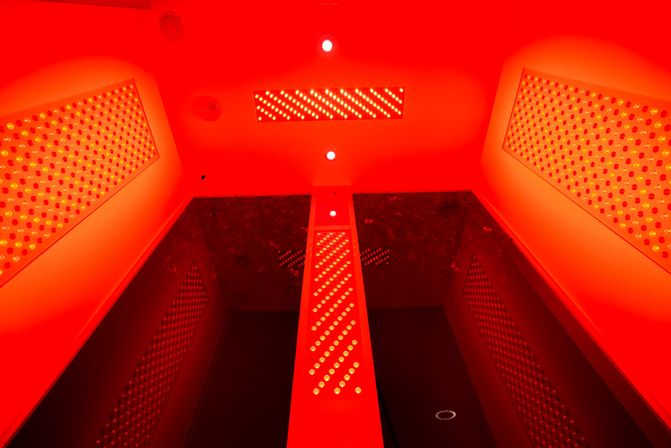 Vibrant red-light therapy chamber interior with ceiling and wall LED panels and reflective glass, viewed looking up.