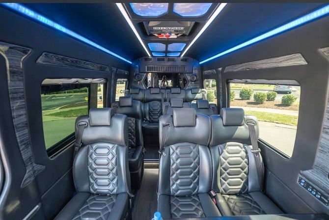 Sleek luxury passenger van interior with black quilted leather captain seats, blue LED ambient lighting, aisle and suburban street view through side windows
