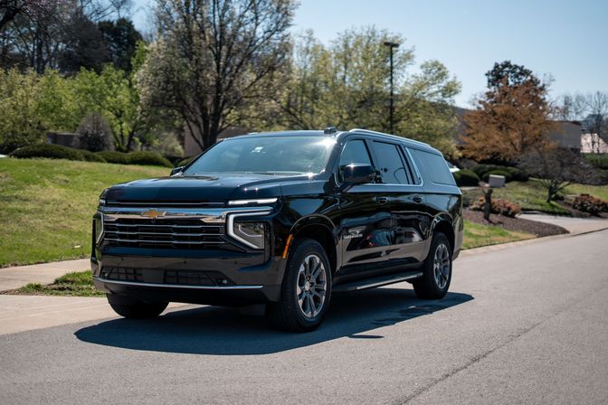 Shiny black Chevrolet Suburban SUV parked curbside in a sunny suburban neighborhood with green lawns and trees