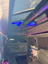 Luxury party limo interior with quilted black leather seats, triangular blue LED ceiling panels, purple neon accent lighting and a built-in bar stocked with champagne flutes