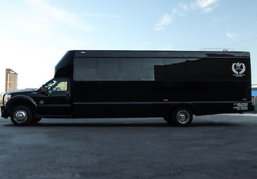 Sleek black shuttle bus with tinted windows parked on an urban street, long side profile under a bright blue sky