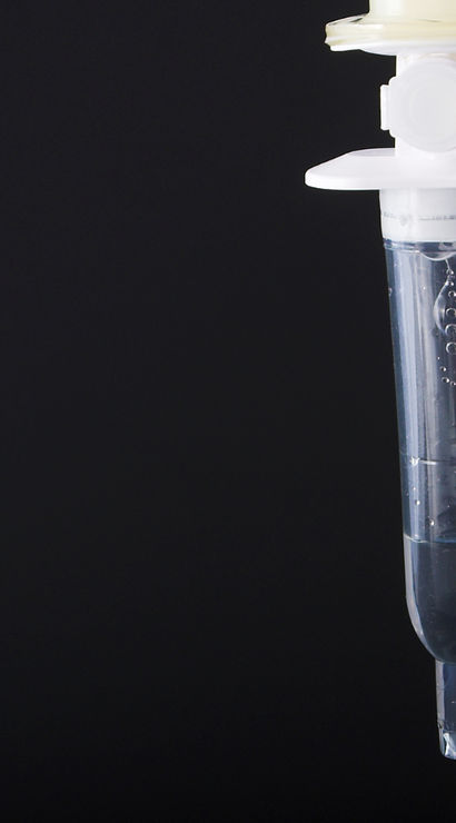Close-up of a clear intravenous (IV) drip chamber with saline and rising air bubbles, tubing hanging against a dark background