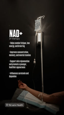 Dimly lit wellness clinic room showing a NAD+ IV therapy bag on a pole and a forearm with an IV catheter resting on a pillow, with promotional bullet points about energy, focus and skin rejuvenation visible on the wall.