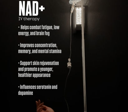 Dimly lit wellness clinic room showing a NAD+ IV therapy bag on a pole and a forearm with an IV catheter resting on a pillow, with promotional bullet points about energy, focus and skin rejuvenation visible on the wall.