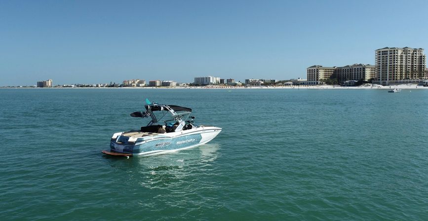 Sunlit motorboat floating on calm turquoise sea off a sandy beach lined with resort condominiums under a clear blue sky