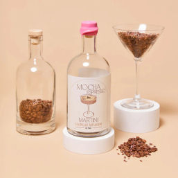 Mocha Espresso Martini cocktail infusion bottle with pink wax seal, glass jars and martini glass filled with coffee beans on a beige background, scattered beans in foreground