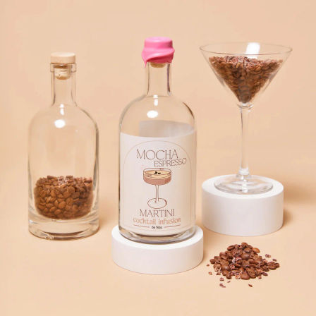 Mocha Espresso Martini cocktail infusion bottle with pink wax seal, glass jars and martini glass filled with coffee beans on a beige background, scattered beans in foreground