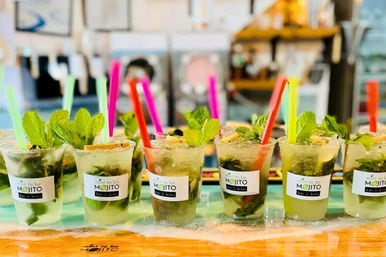 Row of refreshing mojito cocktails in clear cups, garnished with fresh mint, lime wedges and colorful straws on a bright bar counter