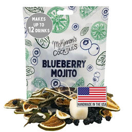 Pouch of Blueberry Mojito cocktail mix surrounded by dried lime slices, dried blueberries and mint leaves with an American flag “Handmade in the USA” label — American-made cocktail mix.