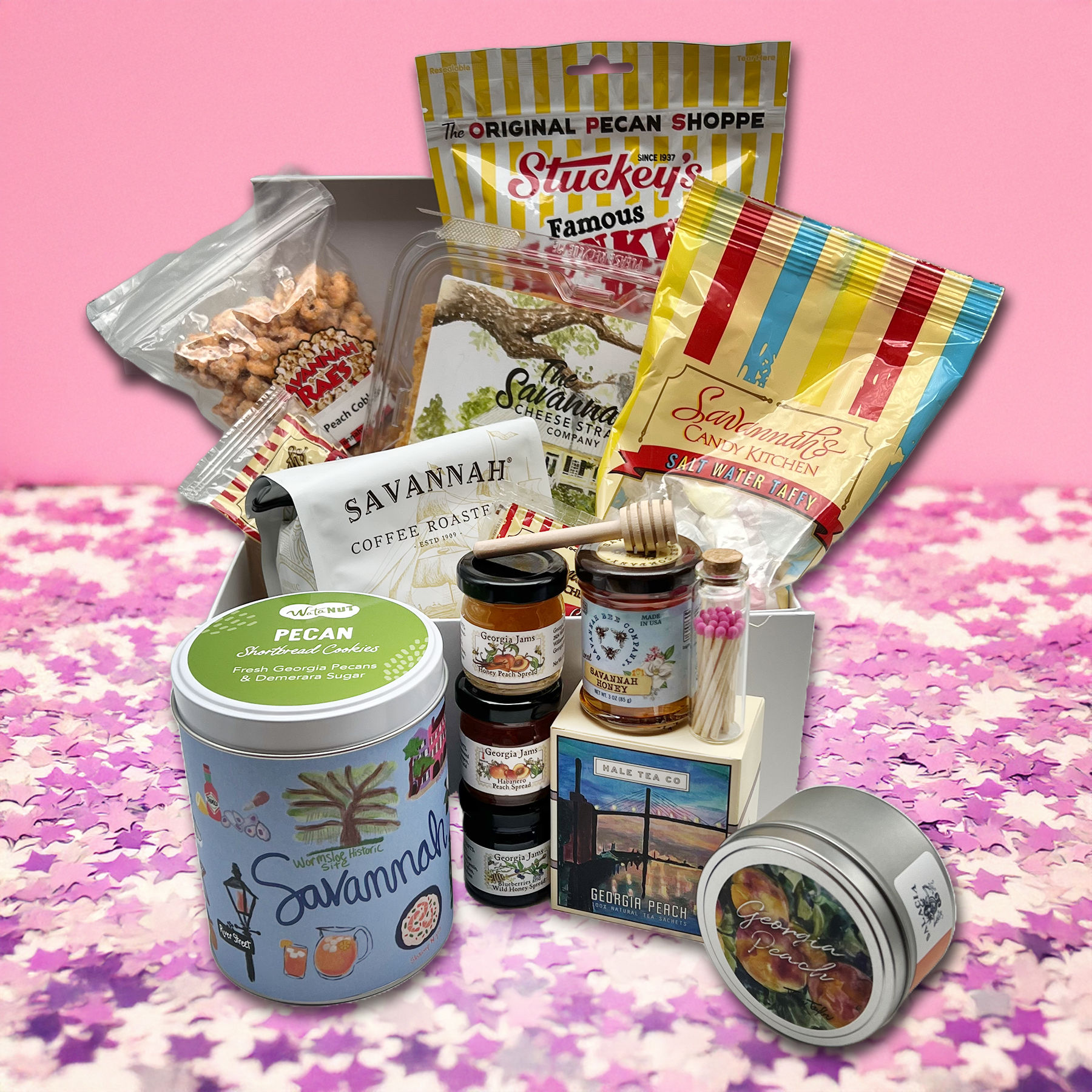Savannah-themed Georgia gift box of Southern treats — pecans, coffee, honey, jams, salt-water taffy and candies arranged on a pink patterned backdrop.
