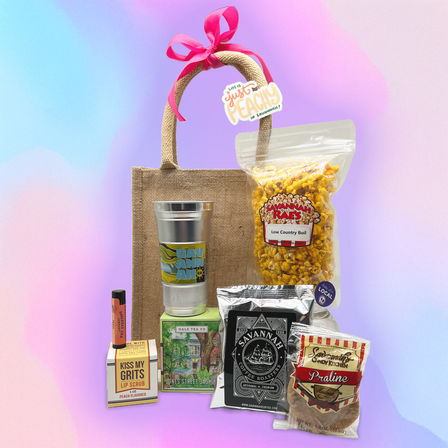 Jute gift tote tied with a pink bow filled with southern snacks and treats — seasoned popcorn, coffee pouch, praline candy, tea box, metal tumbler and peach lip scrub — Savannah, GA souvenir gift set