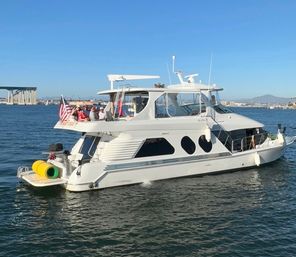 White motor yacht with passengers and American flag cruising San Diego Bay near the Coronado Bridge on a sunny day, city skyline and distant hills in the background