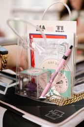 Clear plastic goody bag on a table containing a pink pen, pastel sticker pack, notecards and a small mint box — event favor/stationery kit