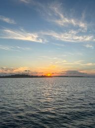 Golden sunset over calm coastal waters with a low island silhouette, rippling sea reflecting the sun and wispy cirrus clouds in a pastel sky.
