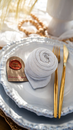 Elegant tablescape: stacked scalloped white plates with a rolled linen napkin, gold cutlery and a wax-sealed birthday place tag