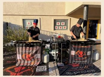 Two chefs sizzling fried rice on outdoor hibachi flat-top grills at a mobile pop-up station, flanked by propane tanks, condiments, and promotional banners.