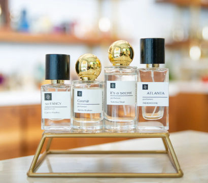 Chic row of four glass perfume bottles with black and gold caps on a brass display stand at a boutique counter, soft blurred shop background