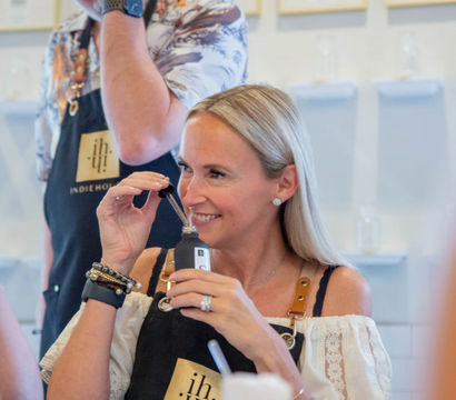 Smiling woman sniffing a dropper of perfume at a hands-on artisan fragrance workshop in a bright studio