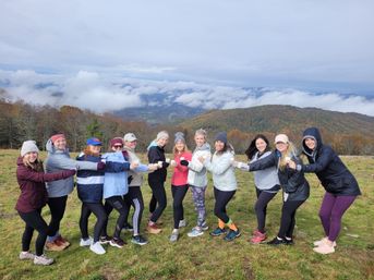 Group of hikers toasting with cups on a misty mountain overlook, autumn-colored hills and low clouds filling the valley