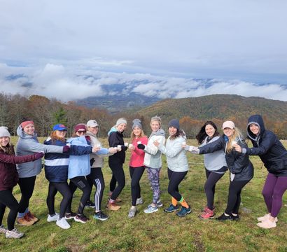 Group of hikers toasting with cups on a misty mountain overlook, autumn-colored hills and low clouds filling the valley