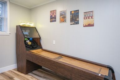 Skee-ball arcade machine in a bright home game room with wooden lane, neon sign, and Nashville "Music City" posters on a pale gray wall