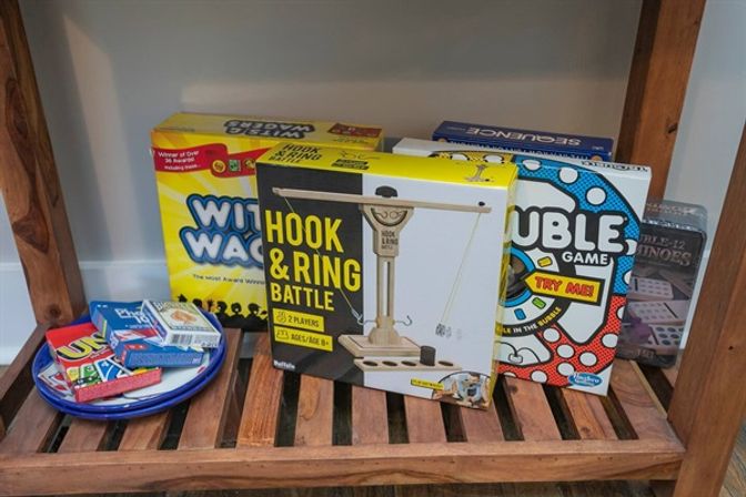 Wooden slatted shelf displaying colorful family games and card decks, featuring a Hook & Ring Battle box, party board game boxes, and a plate stacked with Uno and playing cards.