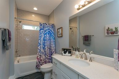 Modern residential bathroom with white subway-tiled tub-shower, vibrant blue-purple mandala shower curtain, white quartz vanity with oval sink and brushed-nickel faucet, large mirror and towel racks.