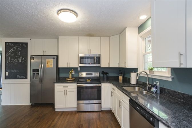 Bright modern Nashville kitchen with white shaker cabinets, stainless-steel fridge, oven and microwave, dark granite countertops, blue-green backsplash, double sink and hardwood floors.